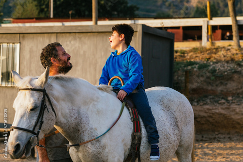 Boy with disabilities having an equine therapy session with a physiotherapist outdoors.