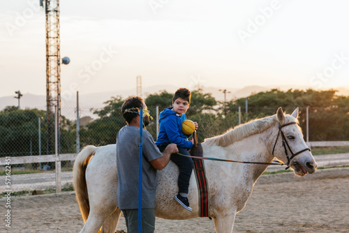 Boy with disability doing exercises with physiotherapist at the equestrian center.
