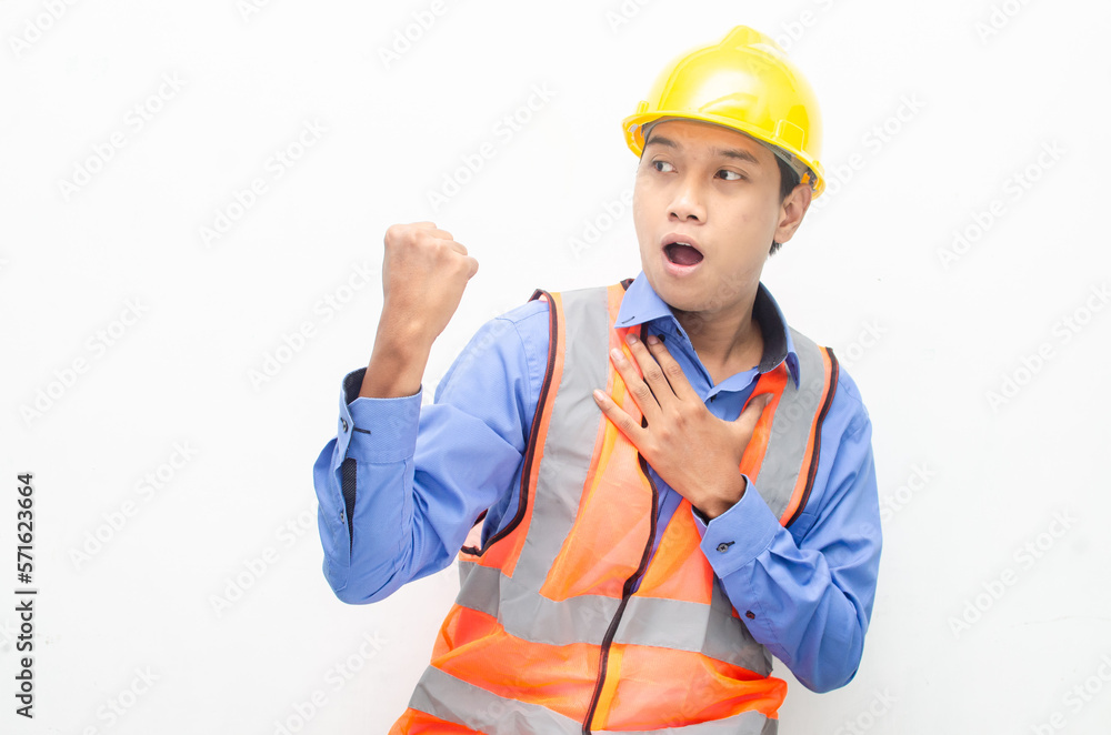 overjoyed asian male construction worker in blue shirt and orange vest with yellow safety helmet doing yes gesture by raising his fist. overjoyed asian male construction worker in blue shirt and orange vest with yellow safety helmet doing yes gesture by raising his fist.