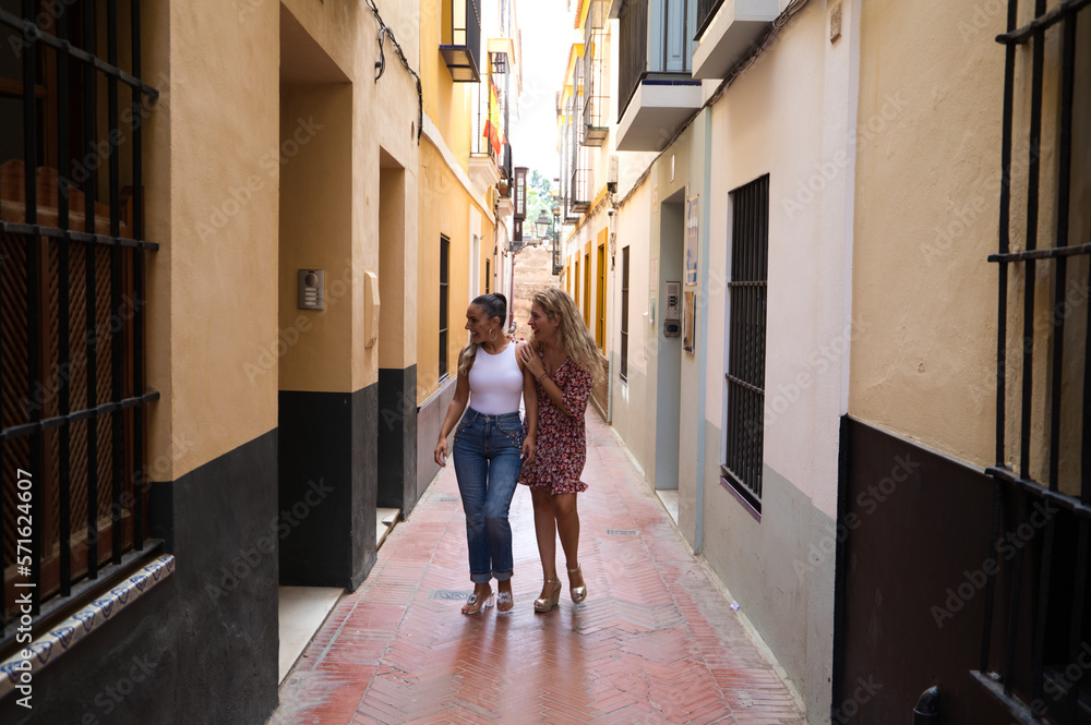 Two beautiful women strolling through the narrow streets of Seville. The women are on vacation in Europe and visit the historical center of the city.