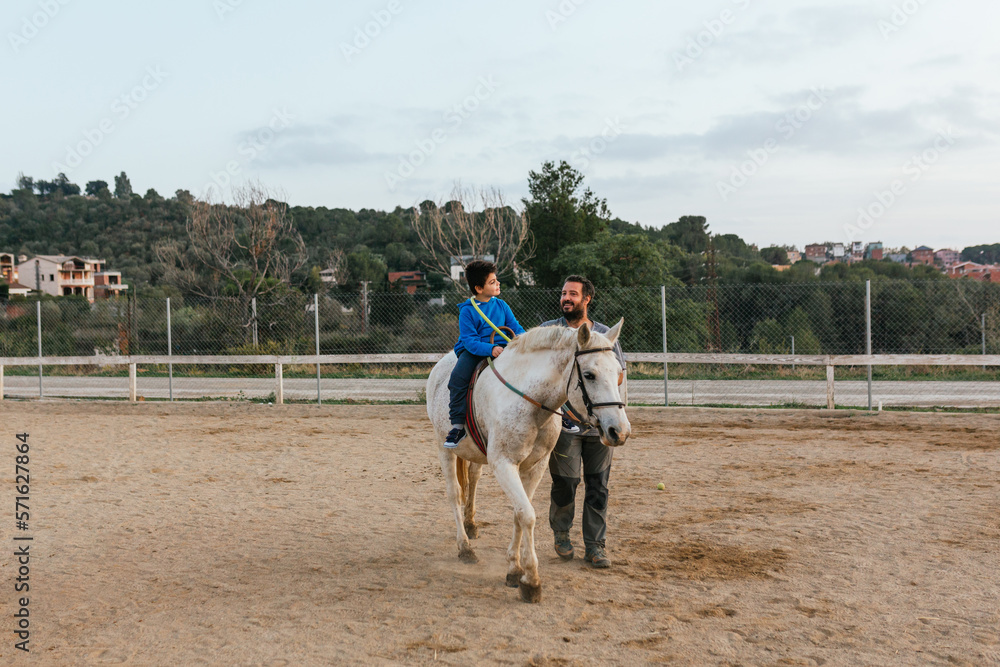 Boy with disabilities doing exercises with a hula hoop during an equine therapy session. Boy with disabilities doing exercises with a hula hoop during an equine therapy session.