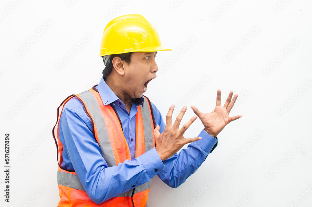 side view of stressed over work concept illustrated by asian male construction worker in blue shirt, orange vest and yellow safety helmet with furious, mad, sad, angry expression. overworked concept side view of stressed over work concept illustrated by asian male construction worker in blue shirt, orange vest and yellow safety helmet with furious, mad, sad, angry expression. overworked concept