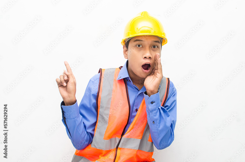 asian construction worker wearing yellow safety helmet and vest smiling and pointing finger with happy and shocked expression. billboard model advertisment concept. 
