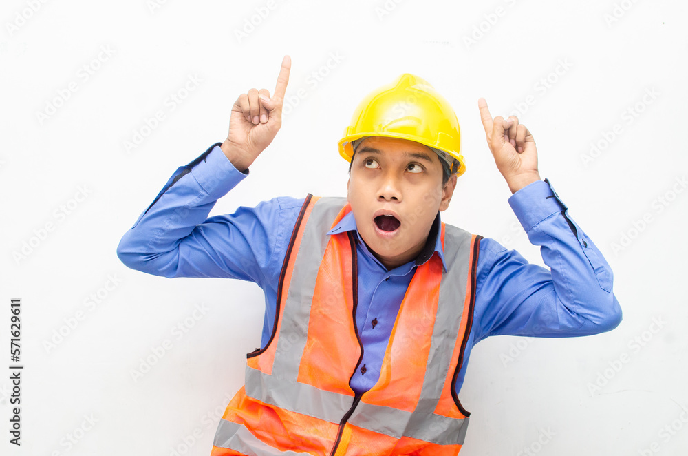 asian construction worker wearing yellow safety helmet and vest smiling and pointing finger with happy and shocked expression. billboard model advertisment concept. 