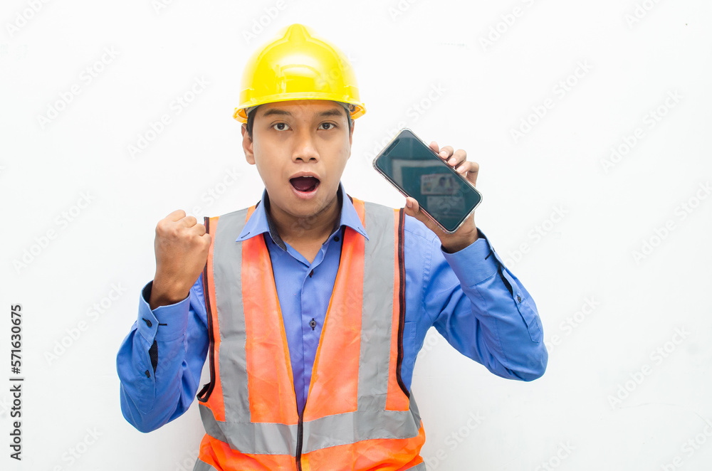 attractive young Asian male construction worker or engineer wearing an orange safety vest and a yellow hardhat holding a phone with shocked, surprised, and amazed expressions. 