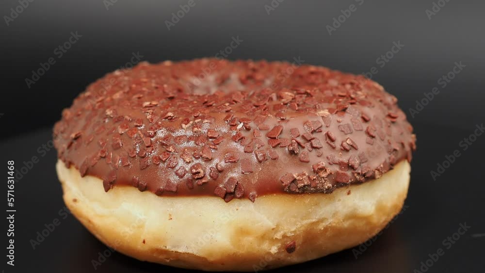 Rotating chocolate donut with chocolate chips on a black background. close-up. Rotating chocolate donut with chocolate chips on a black background. close-up.