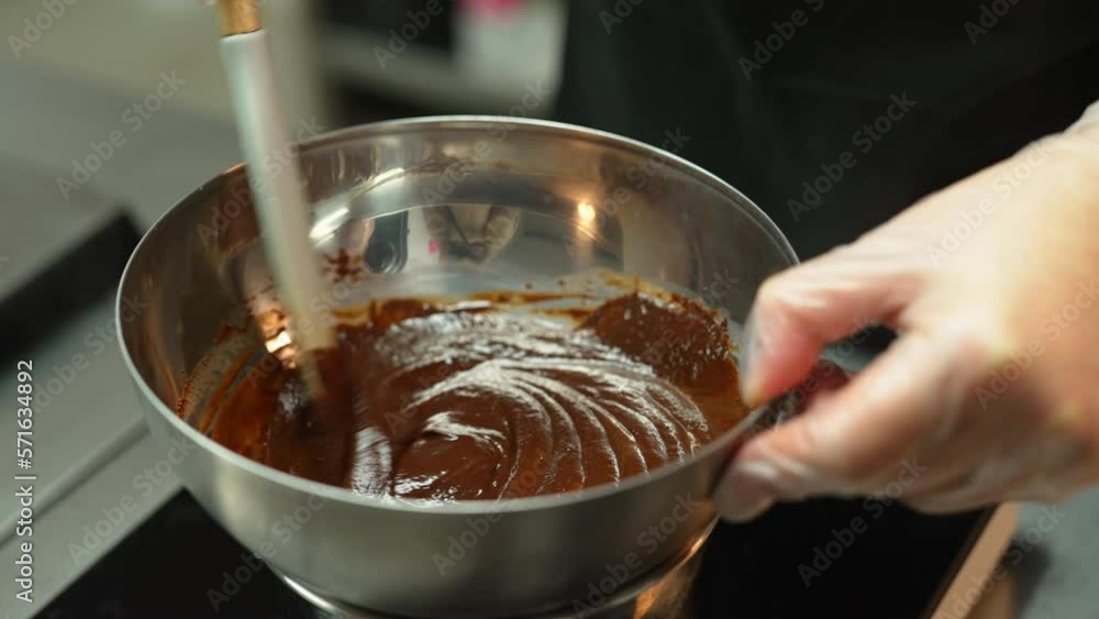 Baker stirring melted chocolate in a metal bowl with a spatula. Blurred background. . High quality 4k footage Baker stirring melted chocolate in a metal bowl with a spatula. Blurred background. . High quality 4k footage