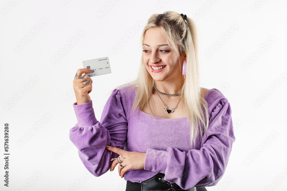 Young blonde girl smiling happy wearing lilac ribbed blouse isolated over white background laughs, looking at the credit card in hand. Excited to shop. Amused or delighted related. Young blonde girl smiling happy wearing lilac ribbed blouse isolated over white background laughs, looking at the credit card in hand. Excited to shop. Amused or delighted related.