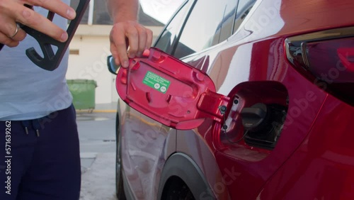 Static shot of crop man in causal clothes opening tank door of red car and removing lip then putting nozzle of pump inside photo