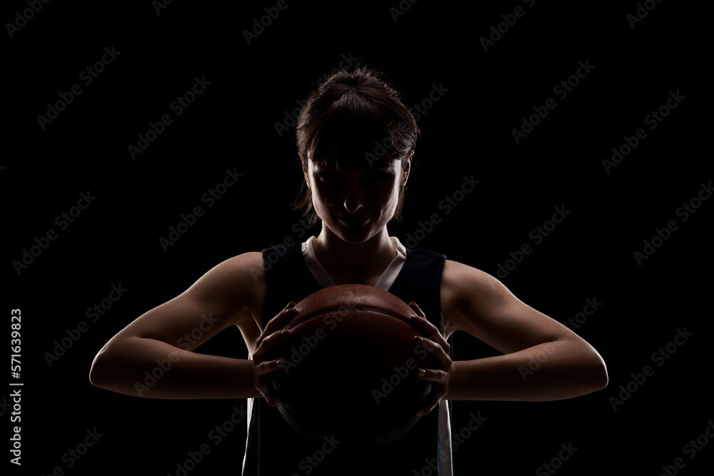 Female basketball player. Beautiful girl holding ball. Side lit half silhouette studio portrait against black background. Female basketball player. Beautiful girl holding ball. Side lit half silhouette studio portrait against black background.