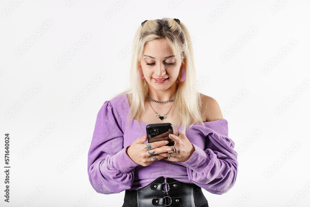 Fototapeta premium Happy woman wearing ribbed blouse standing isolated over white background holding a phone and looking at the screen. Smiling, texting with boyfriend. Using mobile phone, typing sms message.