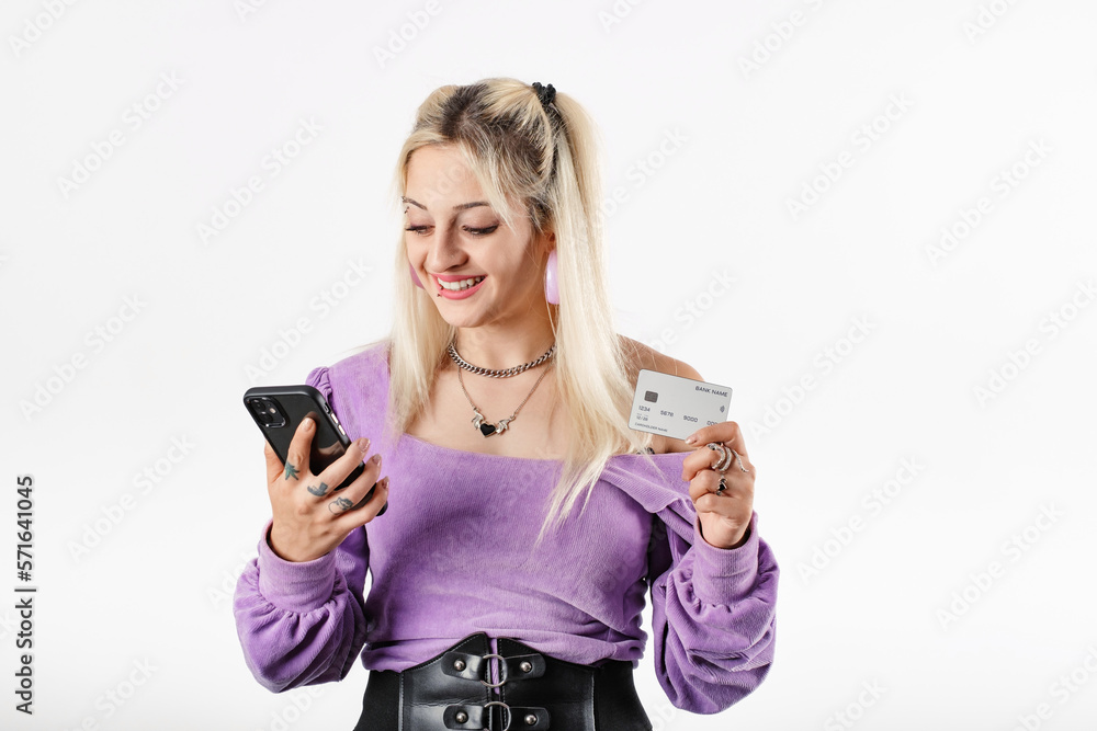 Young woman confident standing isolated over white background holding a credit card in hand, looks at the phone screen, enters card details and makes a purchase. Mobile application advertisement.