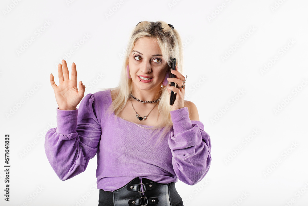 Young blonde woman wearing lilac ribbed blouse isolated over white background talking on the phone and waving palm hand. Looking away.