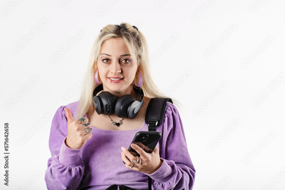 Cute millennial woman wearing blouse standing isolated over white background points at you happily, holds smartphone. Using music app, smiles gladfully. Stands with rucksack or backpack. Cute millennial woman wearing blouse standing isolated over white background points at you happily, holds smartphone. Using music app, smiles gladfully. Stands with rucksack or backpack.