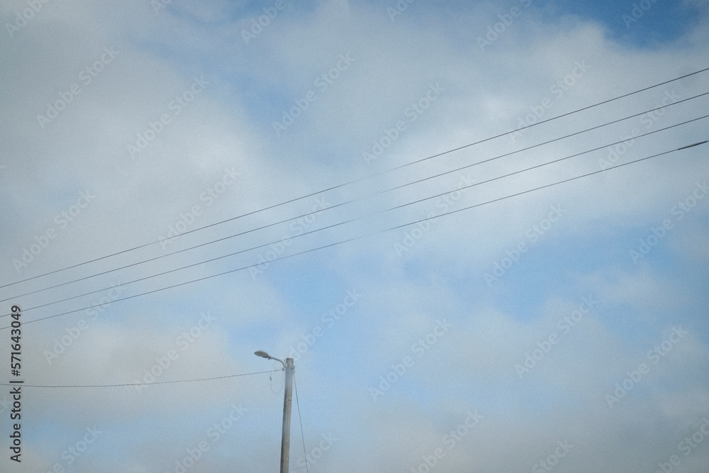 Electric lines and a street light on a background of soft white clouds and light blue sky