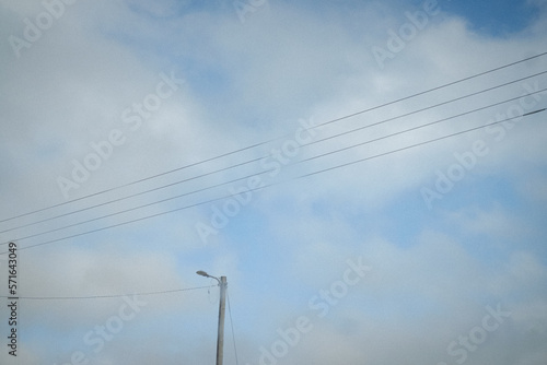 Electric lines and a street light on a background of soft white clouds and light blue sky