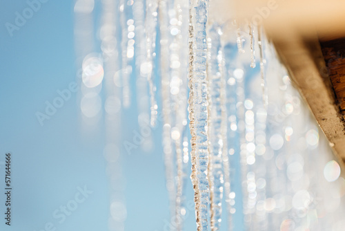 Photo of icicles on the rooftop on the backgrounf blue sky under warm sunlight on the winter, it's shining on a sun. Wintertime and springtime atmosphere with warm sunlight.