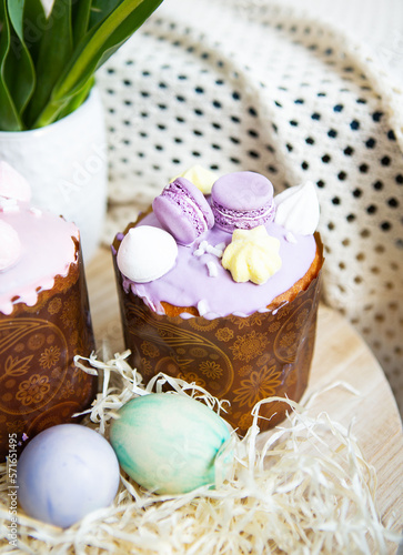 Colorful Easter eggs lie together with Easter pastries decorated with colored chocolate on a wooden table.
