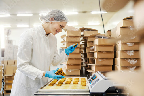 Happy food factory worker is measuring cookies on a scales and preparing to put it in boxes.