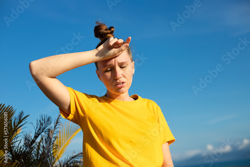 Girl is suffering from heat, woman with heatstroke. Having sunstroke at summer hot weather. Dangerous sun, girl under sunshine. Headache. Person holds hand on head. Feeling bad, unwell, unhealthy photo