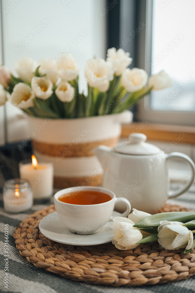 Cup of tea, teapot, basket with tulips, candles in home interior, aesthetic photo Cup of tea, teapot, basket with tulips, candles in home interior, aesthetic photo