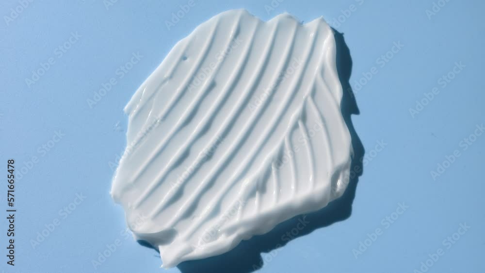 Macro crane shot of white cosmetic cream smear furrow texture on pale blue background | White cosmetic cream commercial Macro crane shot of white cosmetic cream smear furrow texture on pale blue background | White cosmetic cream commercial