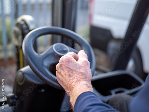Фотография Mans hand on the steering wheel of a fork lift truck in the work place