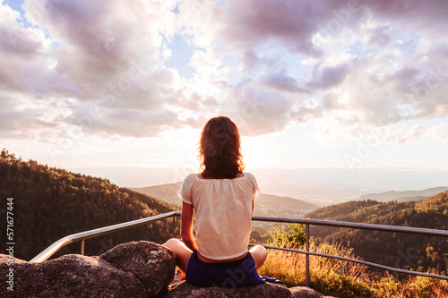 Frau meditierend bei Sonnenuntergang auf einem Berg mit Weitblick und strahlendem Gegenlicht