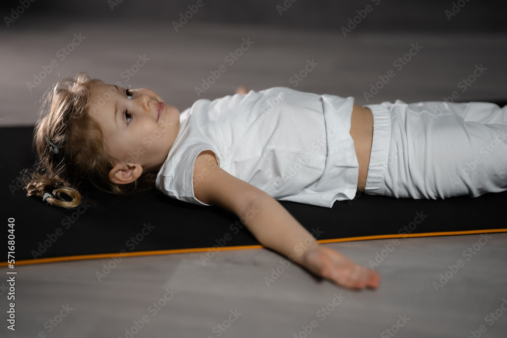 Little girl relax and meditate lying on the mat while practicing yoga in dark room Little girl relax and meditate lying on the mat while practicing yoga in dark room