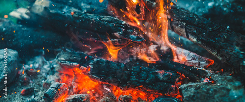 Vivid smoldered firewoods burned in fire close-up. Atmospheric background with orange flame of campfire. Full frame image of bonfire. Warm whirlwind of glowing embers and ashes in air. Sparks in bokeh