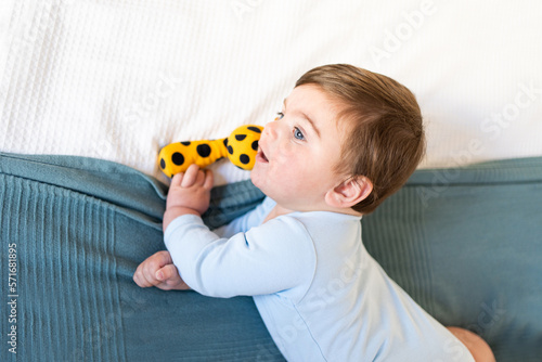 baby on bed with light blue onesie and big blue eyes, blue-gray blanket. little baby playing with yellow stuffed giraffe, top view with copy space