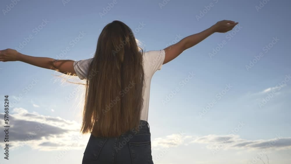 young woman against sky background.Girl stands with raised hands in sunny sky outdoors.girl enjoys freedom, happiness, raising her hands up.woman of freedom happiness, enjoying nature while traveling. young woman against sky background.Girl stands with raised hands in sunny sky outdoors.girl enjoys freedom, happiness, raising her hands up.woman of freedom happiness, enjoying nature while traveling.