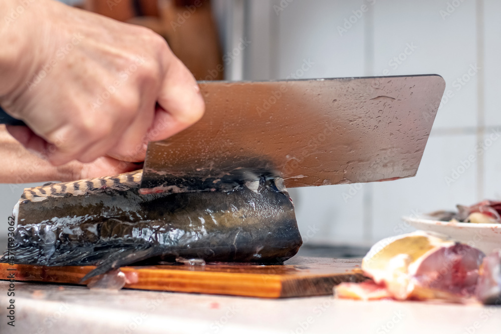 A woman cuts fish with a large knife at home in the kitchen A woman cuts fish with a large knife at home in the kitchen