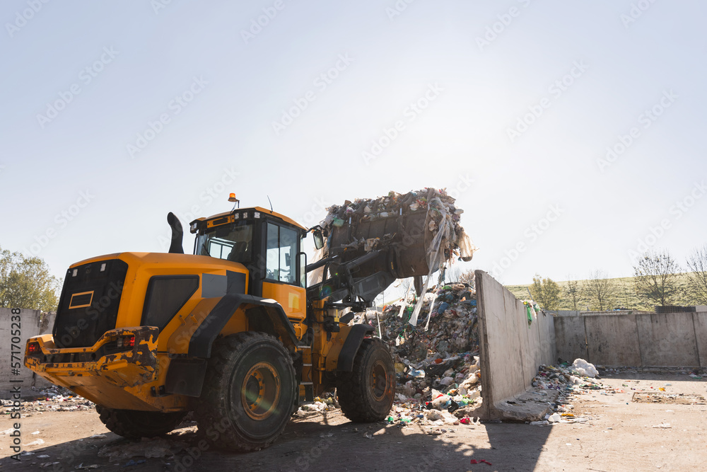 Heavy construction machine, front end loader moving along recycling center area, close up view. Waste management industry concept. Heavy construction machine, front end loader moving along recycling center area, close up view. Waste management industry concept.