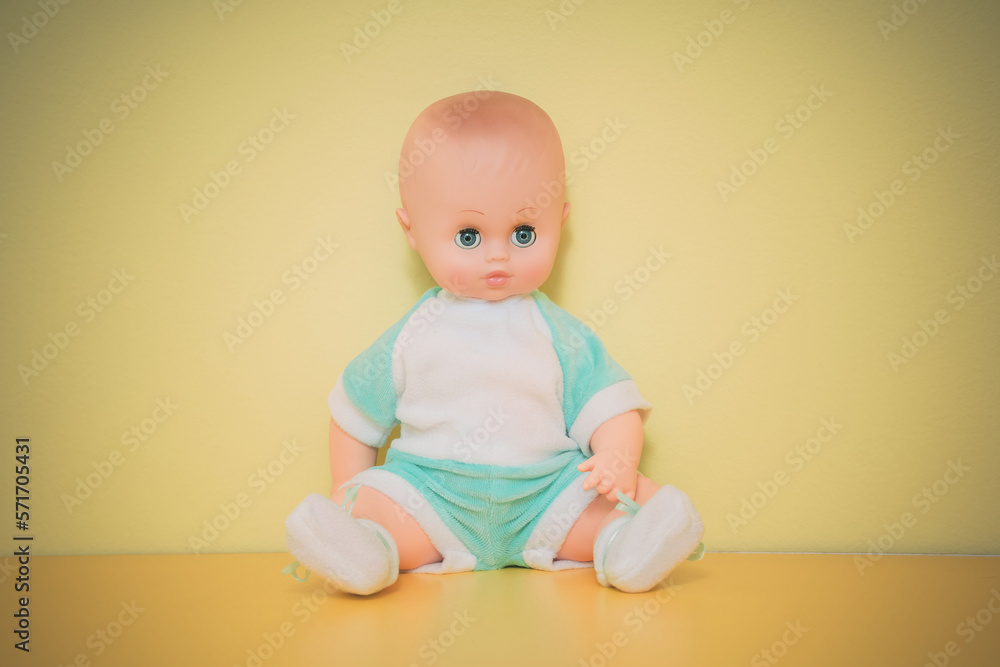 Dressed plastic baby doll sitting on yellow background. Small retro dolly toy for children game. Dressed plastic baby doll sitting on yellow background. Small retro dolly toy for children game.