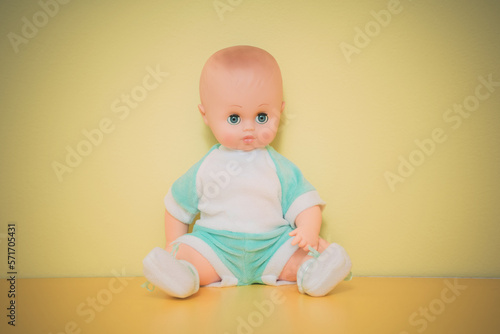Dressed plastic baby doll sitting on yellow background. Small retro dolly toy for children game.