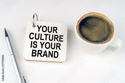 On a white surface, a cup of coffee, a pen and a notepad with the inscription - Your Culture is Your Brand photo