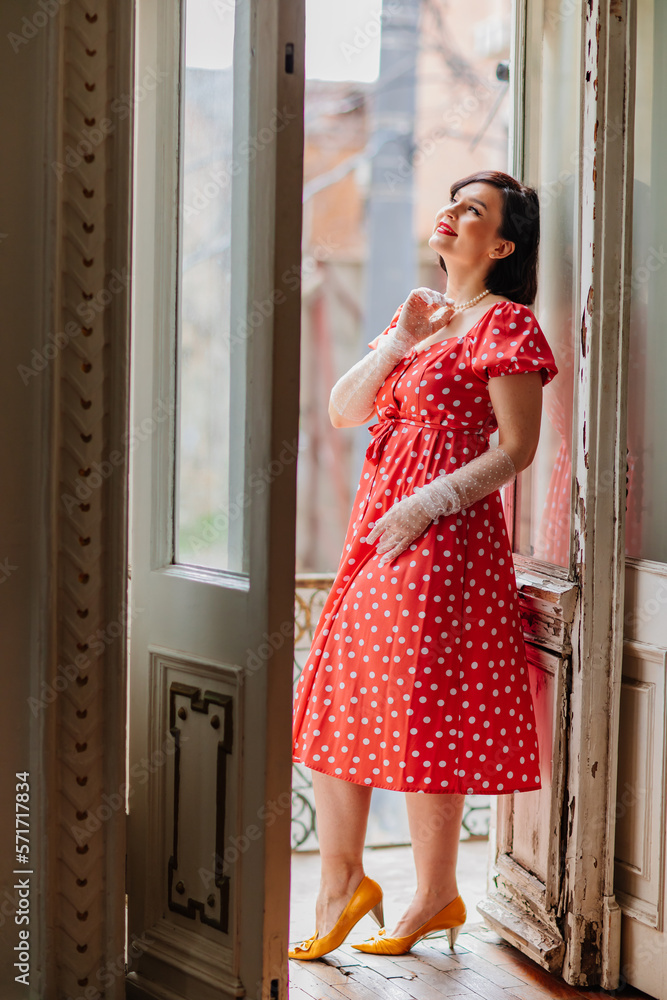 a beautiful and happy brunette women in red retro dress in the balcony doorway a beautiful and happy brunette women in red retro dress in the balcony doorway
