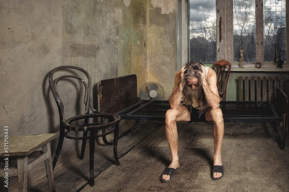 A lonely man in an old room without repair holds his head with his hands A lonely man in an old room without repair holds his head with his hands