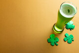 Image of glass with green beer, clover and copy space on orange background