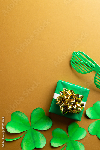 Image of green glasses, green clover, green present and copy space on orange background