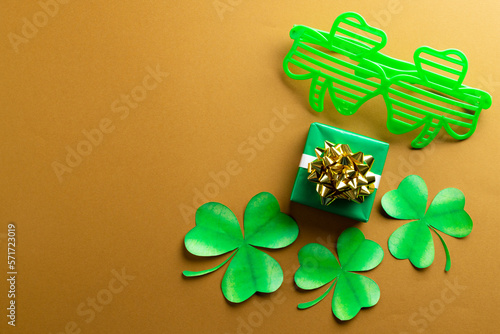 Image of green clover glasses, green clover, green present and copy space on orange background