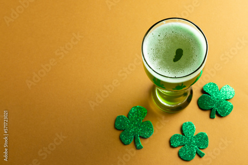 Image of glass with green beer, clover and copy space on orange background