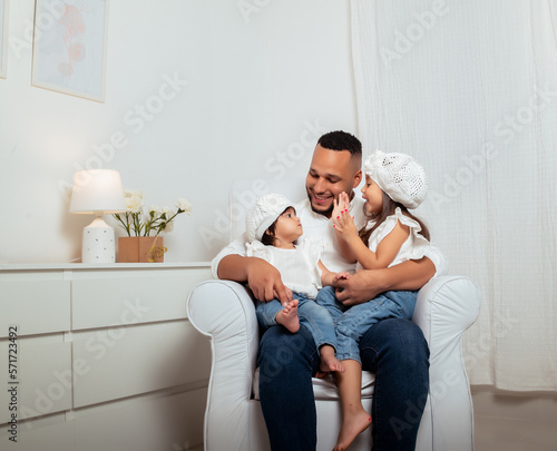 latin father with his daughters playing holding them and smiling sitting on a sofa