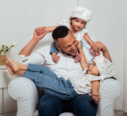  latin father with his daughters playing holding them and smiling sitting on a sofa