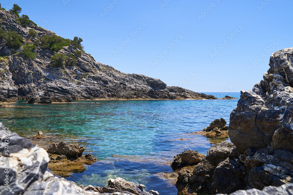 Stony rocks on Ascea beach in the Salerno region of southern Italy. The water of the sea is clear and has a turquoise color. The sky is blue and space for text. Stony rocks on Ascea beach in the Salerno region of southern Italy. The water of the sea is clear and has a turquoise color. The sky is blue and space for text.