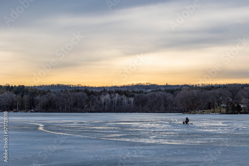 One person ice fishing on a frozen lake on a dark morning.