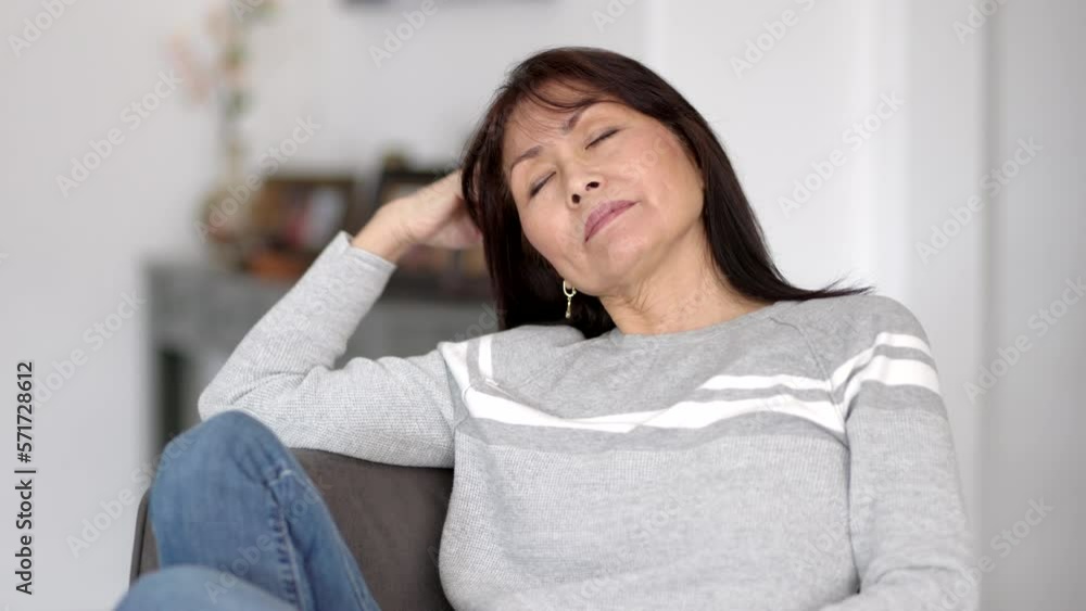 Portrait attractive stylish woman in grey sweater facing camera running fingers through hair sitting on sofa of modern home Portrait attractive stylish woman in grey sweater facing camera running fingers through hair sitting on sofa of modern home