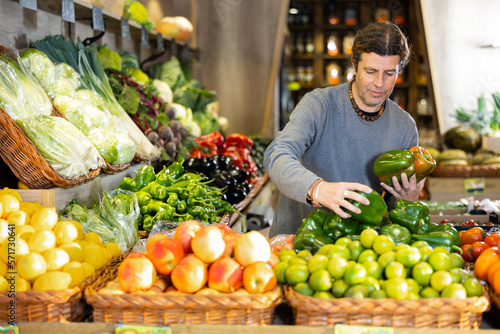 Portrait of positive satisfied man buying fresh bell peppers in grocery shop