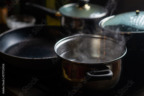 A pot of boiling water on a kitchen stove. Kitchen utensils are nearby.